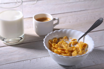 Corn Flakes cereal in a bowl, glass with milk and cap with espresso coffee. Morning breakfast.