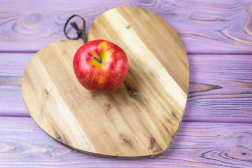 Fresh red apple on a wooden background in the shape of a heart.