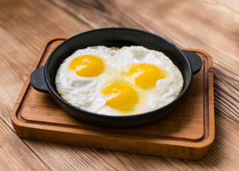 Fried eggs in a frying pan on a wooden background.