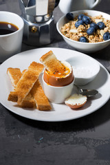 soft boiled egg, toasts and coffee for breakfast on dark background, vertical