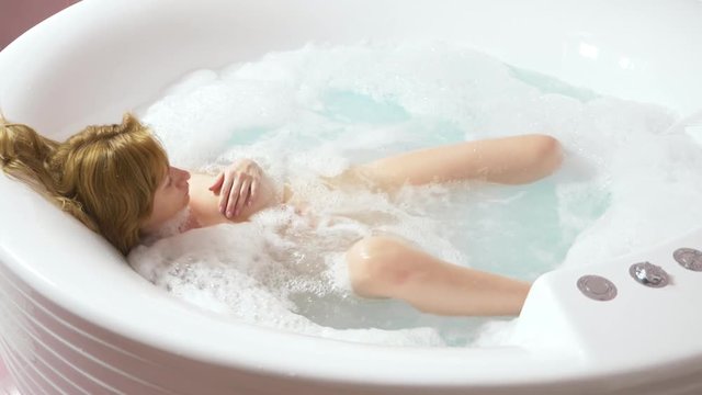 Beautiful young woman relaxes in a bath with hydromassage , on a blue background. Concept: spa procedures, body massage, spa cream, relaxation, water treatments. 4k, slow motion. view from above
