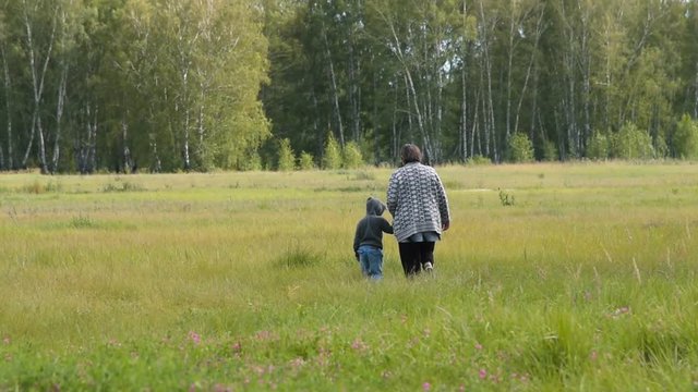 Grandmother and little granson walking in the countryside holding hands. Family leisure outdoor