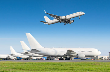 Obraz premium Rząd samolotów pasażerskich, samolot zaparkowany na służbie przed odlotem na lotnisku, inny samolot odepchnął hol. Samolotowy lądowanie pas startowy w niebieskim niebie.