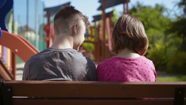 Back view of a couple teenage - teen boy and girl sitting together on the bench outdoors. Friendship and love concept - close-up.
