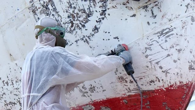 Workers tear off paint on metal in repairs process at shipyard. Working people in overalls reconstruct at ship repair yard outdoors in port.
