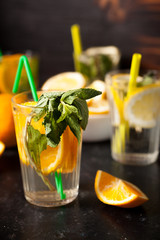 Glasses with natural water with slices of oranges and lemons in it on dark vintage wooden background