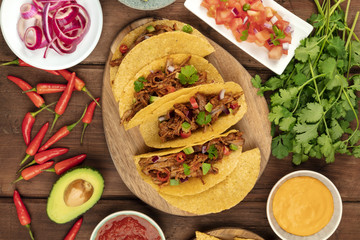 Overhead photo of Mexican tacos with pulled meat, avocado, chili peppers, cilantro, cheese sauce