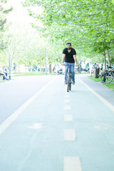 Young bearded man riding a bicycle in the park in summer