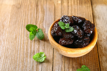Prunes with mint leaves in a bowl on an old wooden table.