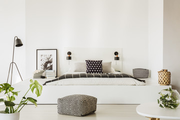 Real photo of spacious, scandi bedroom interior with patterned pouf in front of a bed on a platform...