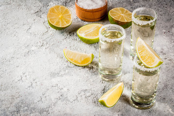 Tequila shots with lime and sea salt on grey stone table, copy space