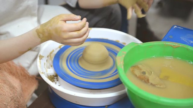 The teacher helps the child to work with clay on the potter's wheel.