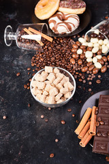 Brown sugar in a glass bowl next to candies and sweets on dark vintage wooden background