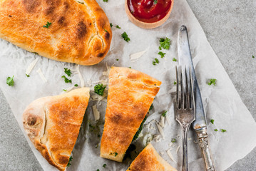 Italian food, closed pizza calzone with Spinach and Cheese, gray stone background, copy space top view