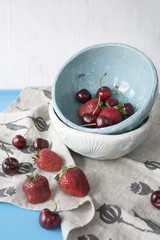 Blue plates with red juicy strawberries and delicious cherries on a blue wooden background.