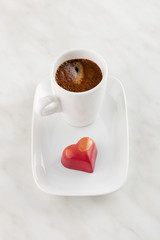Red heart shaped handmade chocolate candy on plate with cup of coffee espresso