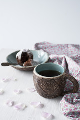 Clay cup with blue in the middle and a plate with a cupcake in the background. Items are on a white wooden background.