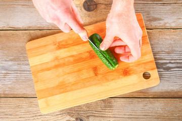 Men's hands cut the light for okroshki on a cutting board on an old wooden table.
