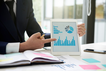 Asian business man analyze and discuss the situation on the marketing data online and calculate...