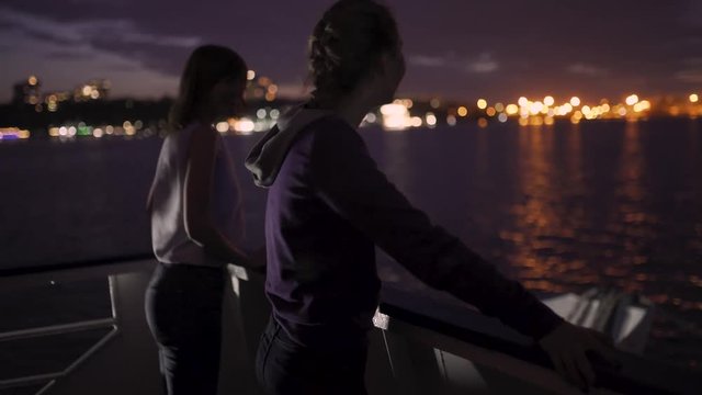 Silhouette of two attractive young women traveling on a ship at night. Girlfriends on the boat