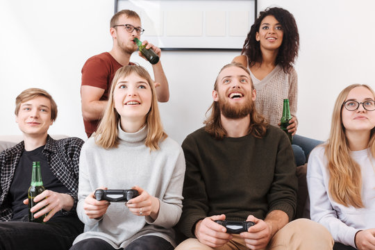 Close up photo of cheerful friends sitting on sofa and spending time together while playing video games and drinking beer at home