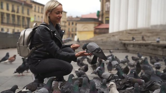 Beautiful young woman feeding pigeons on the street