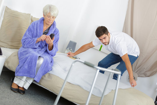 senior woman with walking frame while caretaker making her bed