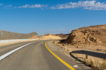 Asphalt road and fence wall on boarder with Egypt in desert Negev, Israel, road 12, transport...