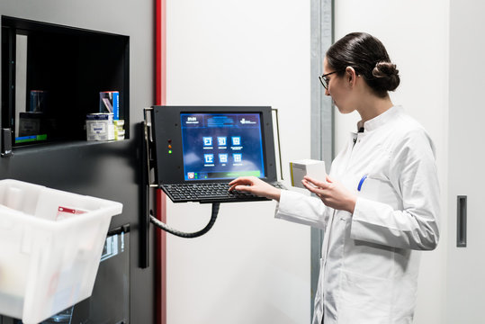 Low-angle rear view of an experienced female pharmacist using a computer while managing the drug stock in a contemporary pharmacy with modern technology