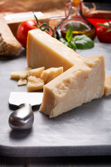 Traditional italian food - aged Italian parmesan hard cheese Parmigiano-Reggiano with cheese knife, tomato, basil, olive oil