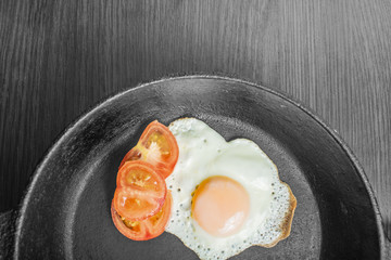 fried egg with tomatoes in a cast-iron frying pan on a wooden table