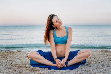 Fototapeta na wymiar Pregnant woman practicing yoga at beach at dawn