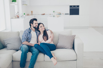 Obraz premium Portrait of attractive cheerful couple spending time together indoor, in house, apartment sitting on sofa looking to the side. True feelings harmony idyllic affection concept