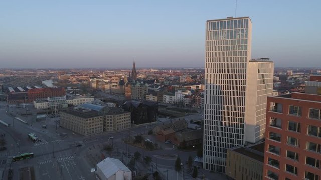 Drone shot flying by modern skyscraper office buildings and up over Malmö city, Sweden. Aerial view of Malmoe cityscape skyline at sunset