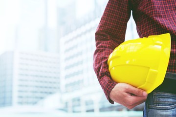 Close up front view of engineering male Plaid shirt construction worker holding safety yellow helmet for the safety of the work operation. outdoor of building background.