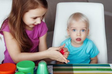 Two happy children Blond boy and girl playing sitting at table at home
