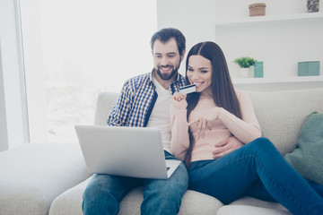 Portrait of clients, stylish shopaholics, modern couple having plastic credit discount card in hand spending earnings in internet store using laptop enjoying fast shopping looking goods