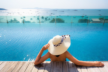 Fototapeta na wymiar Sexy Woman in Swimsuit is Relaxing in Swimming Pool on The Deck Floor and Landscape Scenery View of The Beach, Beautiful Asian Woman Wearing Straw Hat and Relax Sunbathe in Poolside on Summer Holiday.