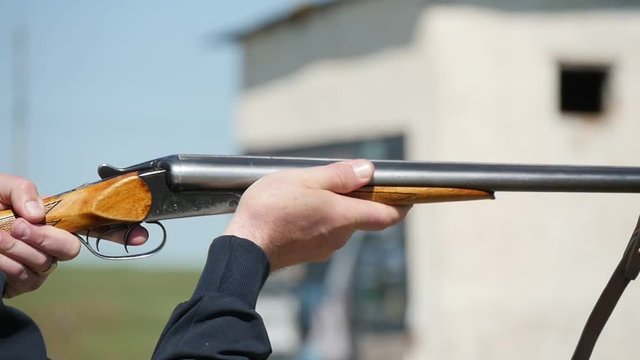 Closeup of a man keeping his old but reliable shortgun, targeting and shooting at clay targets. The recoil shakes the rifle on a range in slo-mo