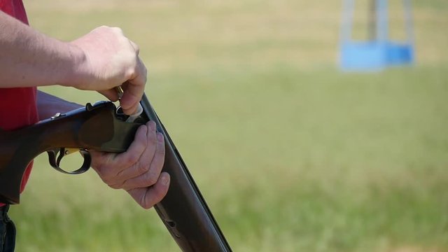 Closeup of a sportman opening the breech of his double barrel shortgun, loading it with cartridges and closing the breech mechanism in summer 