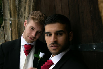 Gay wedding, grooms posing for as they hold hands and kiss outside village church