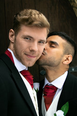 Gay wedding, grooms posing for as they hold hands and kiss outside village church