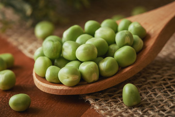 Fresh raw green peas in wooden spoon on table