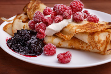 tasty home made pancakes with ice cream on craft wood table decorated with jam, raspberries and nuts