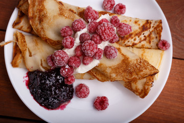 tasty home made pancakes with ice cream on craft wood table decorated with jam, raspberries and nuts