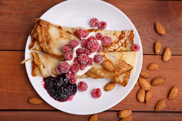 tasty home made pancakes with ice cream on craft wood table decorated with jam, raspberries and nuts