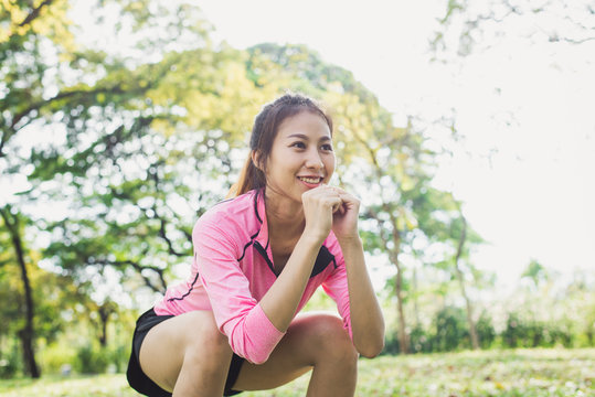 Young asian woman do squats for exercise to build up her beauty body in park environ with green trees and warm sunlight in the afternoon. Young woman workout exercise at the park. Outdoor exercising.