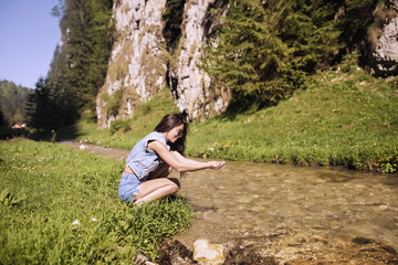 Naklejka na ściany i meble A beautiful tourist enjoys nature next to a mountain river