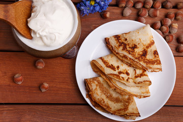 tasty home made pancakes with jar of sour cream on craft wood table decorated with nuts and flower