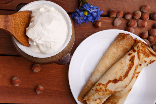 tasty home made pancakes with jar of sour cream on craft wood table decorated with nuts and flower